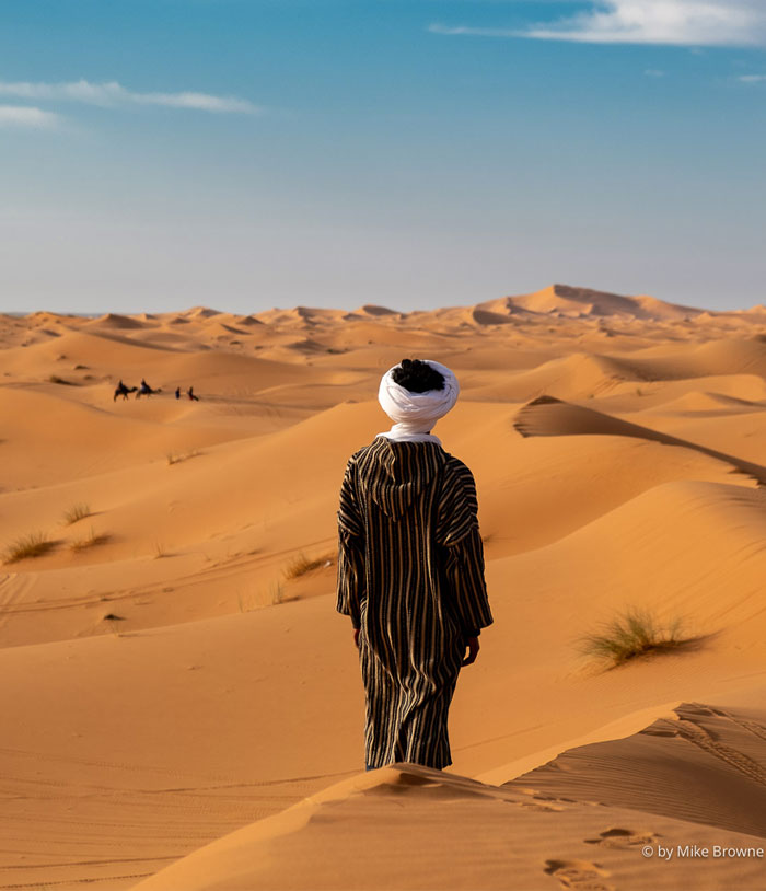 Sharah desert sand dunes. Man facing away, camels and rides in distance